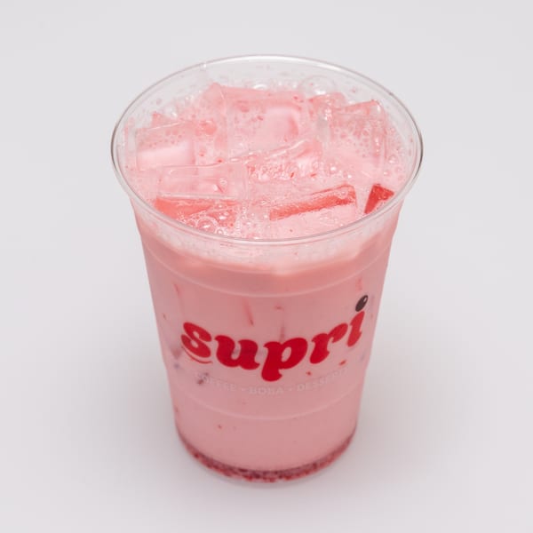 A Supri branded plastic cup filled with a pink, icy strawberry drink, with strawberry bits at the bottom.