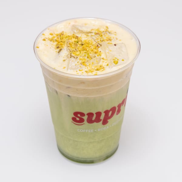 Iced matcha latte with a creamy foam topping and crushed pistachios in a clear plastic cup.