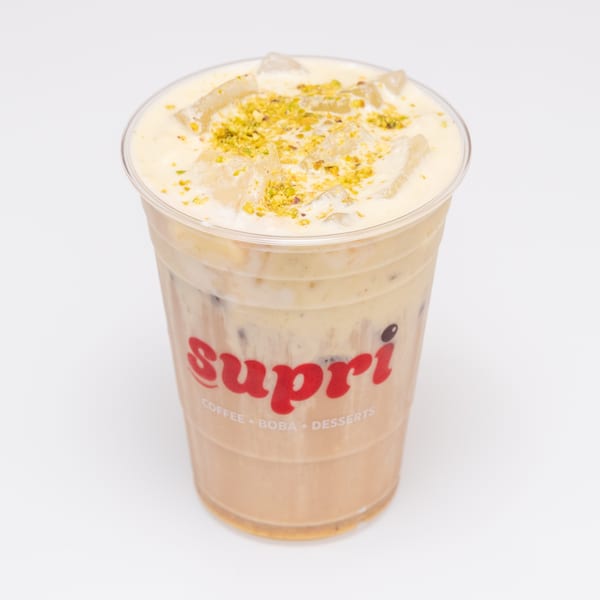 Iced Supri coffee drink with creamy topping and pistachio sprinkles in a clear plastic cup.