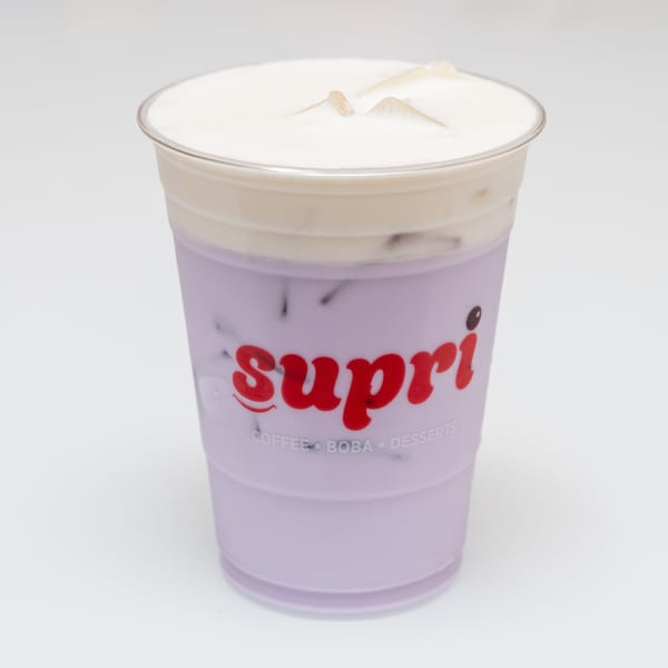 A Supri taro boba tea with a creamy foam topping and ice in a clear plastic cup.