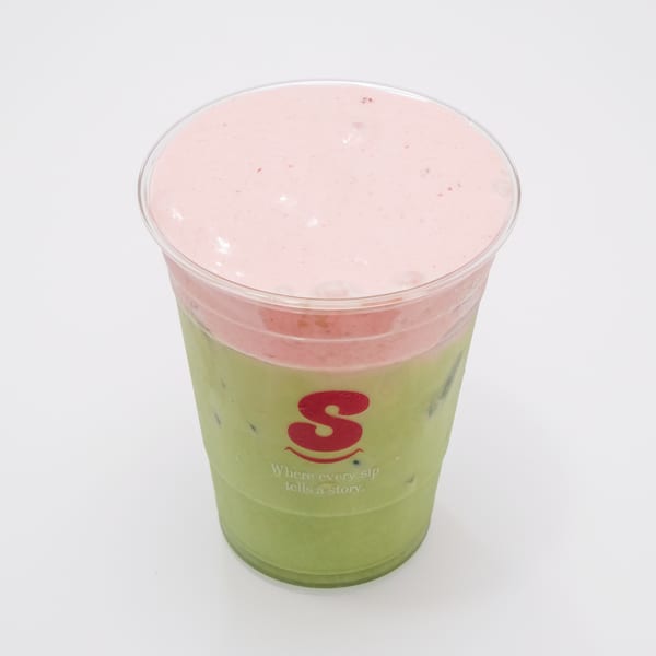 A clear plastic cup with a green drink topped with pink foam, featuring a red 'S' logo.