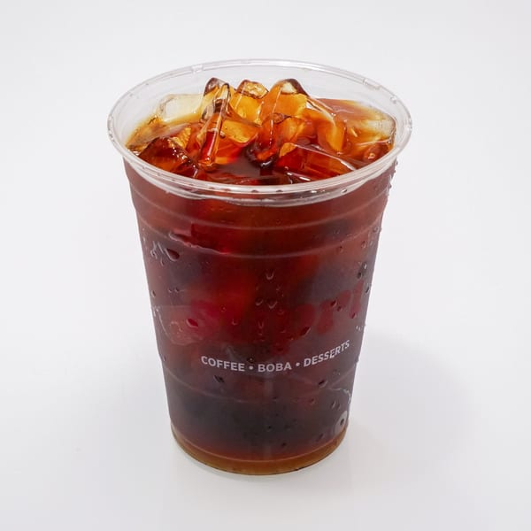 Iced coffee in a clear plastic cup with "COFFEE • BOBA • DESSERTS" printed on it.